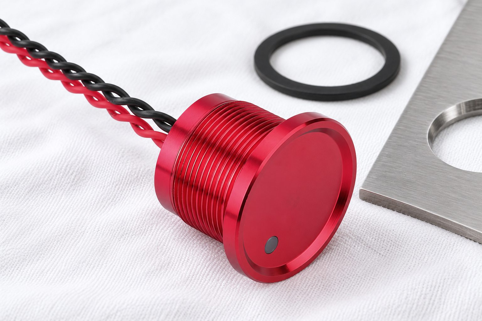 Washdown piezo switch evaluation body1 All-red threaded piezo button with flat red face, small gray indicator dot and twisted insulated red and black rear leads, disconnected on a dry stainless inspection surface
